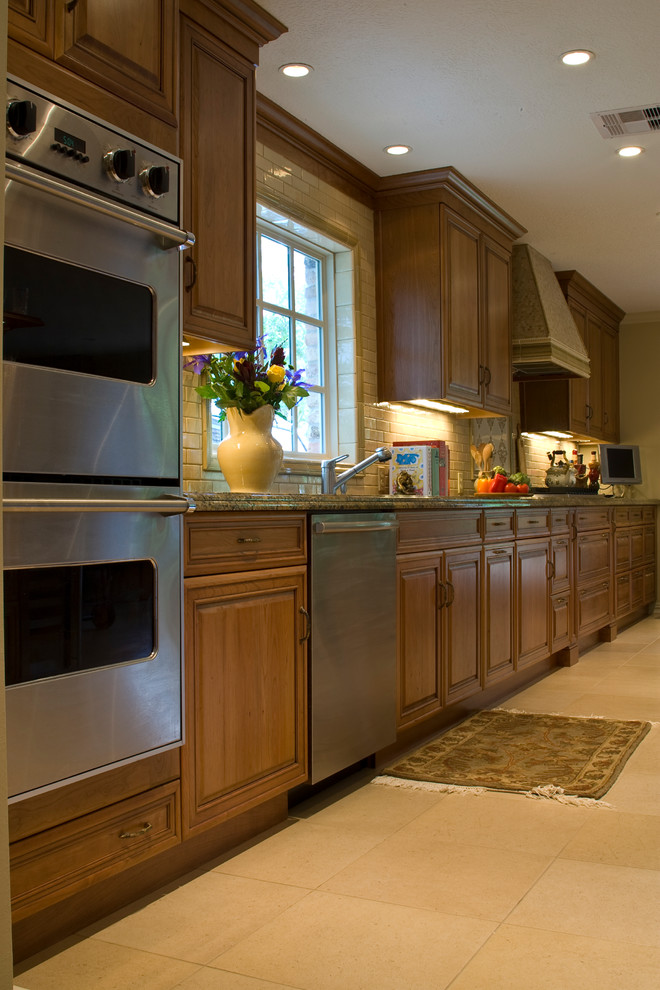 Cette photo montre une cuisine ouverte linéaire chic en bois brun de taille moyenne avec un évier encastré, un placard avec porte à panneau surélevé, un plan de travail en granite, une crédence beige, une crédence en céramique, un électroménager en acier inoxydable, un sol en carrelage de porcelaine, îlot et un sol beige.