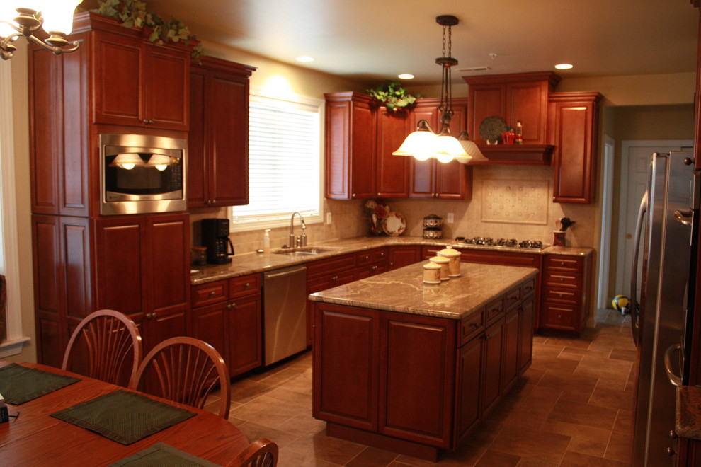 Klassisk inredning av ett kök, med en undermonterad diskho, luckor med upphöjd panel, röda skåp, granitbänkskiva, beige stänkskydd, stänkskydd i keramik och rostfria vitvaror