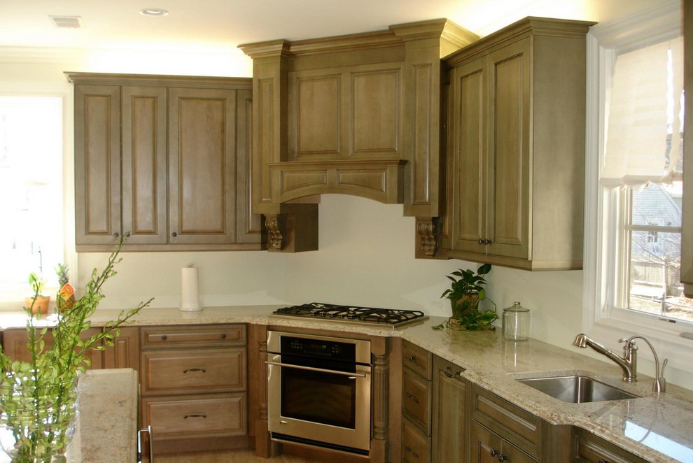 Inredning av ett klassiskt kök, med en dubbel diskho, luckor med upphöjd panel, skåp i ljust trä, granitbänkskiva, beige stänkskydd, stänkskydd i stenkakel, rostfria vitvaror, mellanmörkt trägolv och en köksö