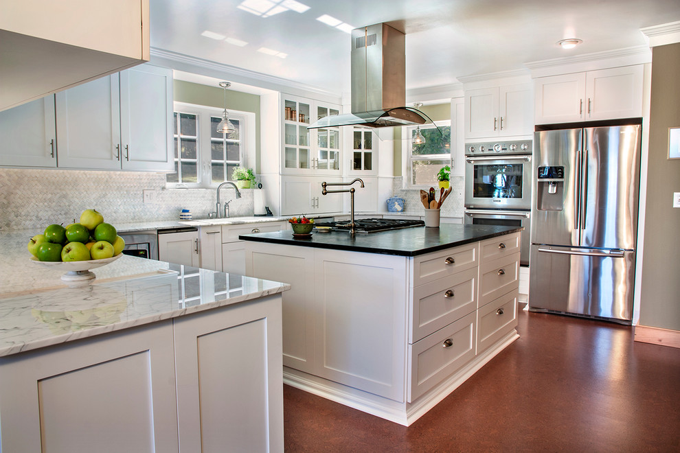 Modelo de cocina tradicional con armarios estilo shaker, puertas de armario blancas, salpicadero blanco, electrodomésticos de acero inoxidable y salpicadero de azulejos de piedra