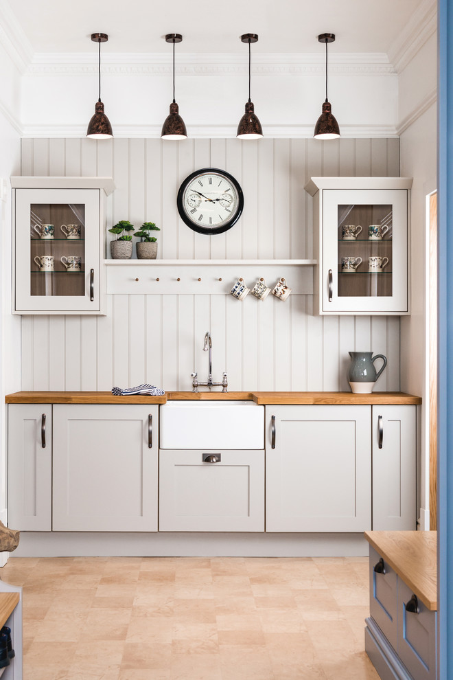 Réalisation d'une cuisine linéaire champêtre avec un évier de ferme, un placard à porte shaker, des portes de placard grises, un plan de travail en bois, un électroménager blanc, un sol beige et un plan de travail marron.