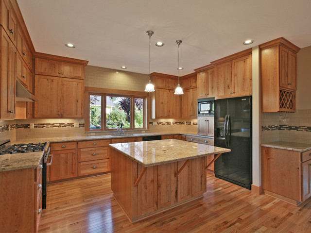 Exempel på ett avskilt, mellanstort klassiskt u-kök, med en undermonterad diskho, skåp i shakerstil, skåp i mellenmörkt trä, granitbänkskiva, beige stänkskydd, stänkskydd i keramik, svarta vitvaror, mellanmörkt trägolv och en köksö
