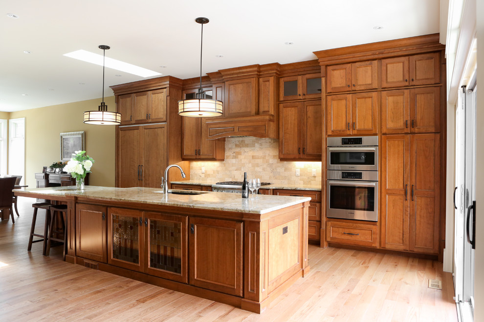 Klassisk inredning av ett stort linjärt kök med öppen planlösning, med en undermonterad diskho, luckor med infälld panel, skåp i mellenmörkt trä, granitbänkskiva, beige stänkskydd, stänkskydd i keramik, rostfria vitvaror, ljust trägolv och en köksö