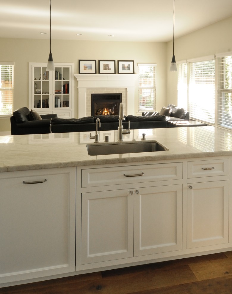 Klassisk inredning av ett stort kök, med en undermonterad diskho, luckor med infälld panel, vita skåp, bänkskiva i kvartsit, beige stänkskydd, stänkskydd i keramik, rostfria vitvaror, mellanmörkt trägolv och en halv köksö