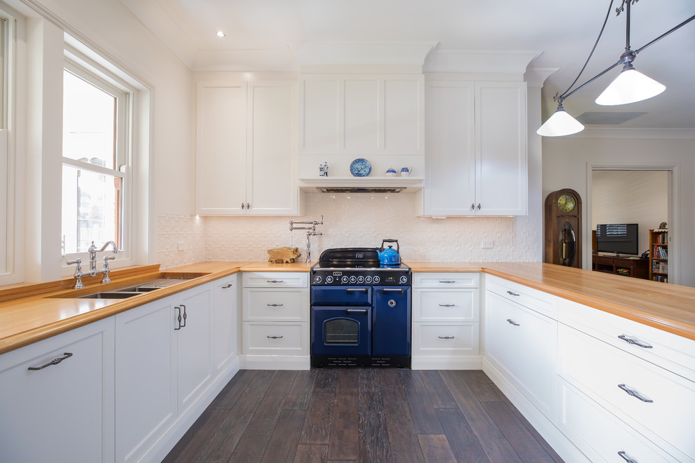 This is an example of a large classic u-shaped open plan kitchen in Adelaide with a double-bowl sink, recessed-panel cabinets, white cabinets, wood worktops, white splashback, metal splashback, coloured appliances, dark hardwood flooring, a breakfast bar and brown floors.