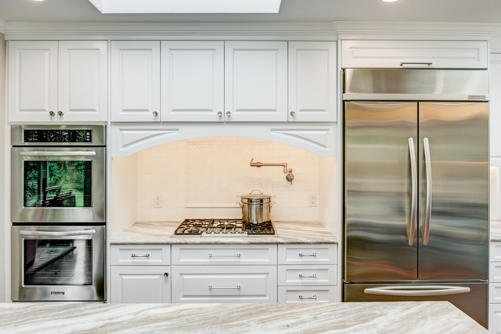 Photo of a large country u-shaped open plan kitchen in San Francisco with a belfast sink, raised-panel cabinets, white cabinets, engineered stone countertops, beige splashback, metro tiled splashback, stainless steel appliances, medium hardwood flooring, an island and brown floors.