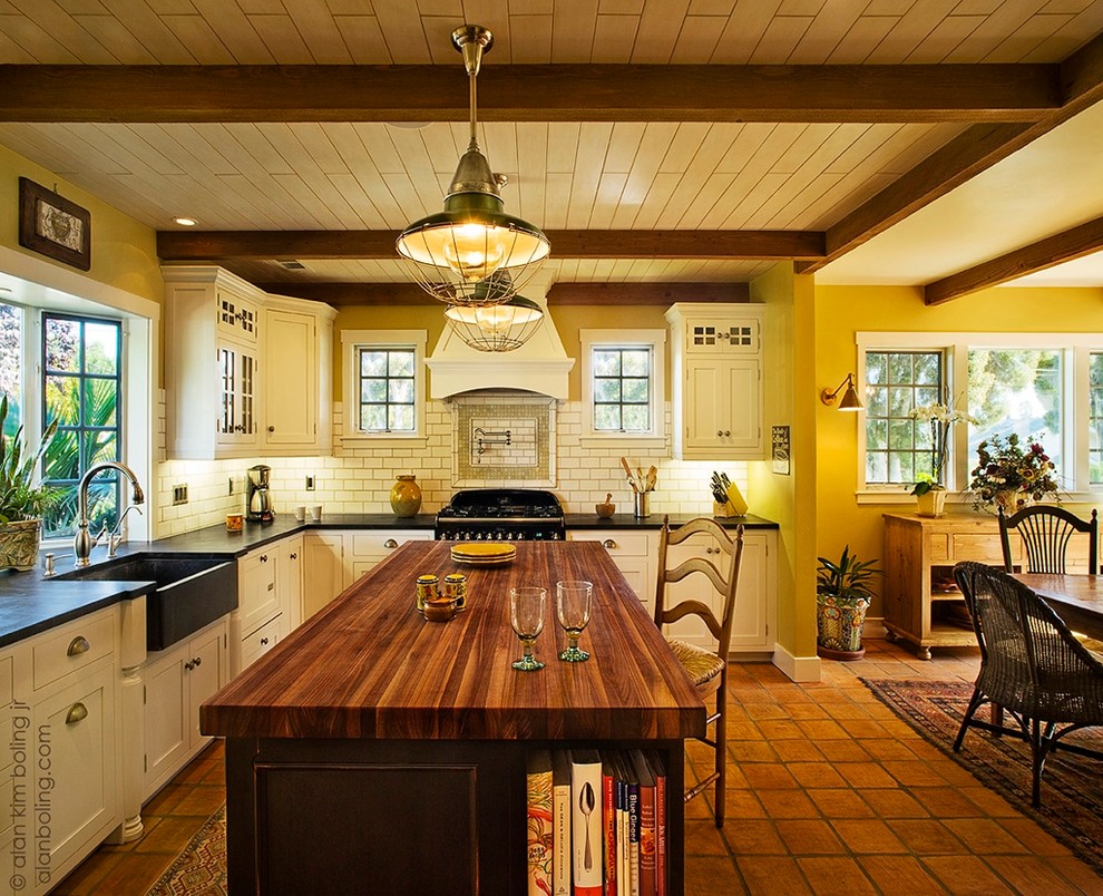 Enclosed kitchen - large traditional u-shaped terra-cotta tile enclosed kitchen idea in Santa Barbara with a farmhouse sink, recessed-panel cabinets, white cabinets, wood countertops, white backsplash, subway tile backsplash, black appliances and an island