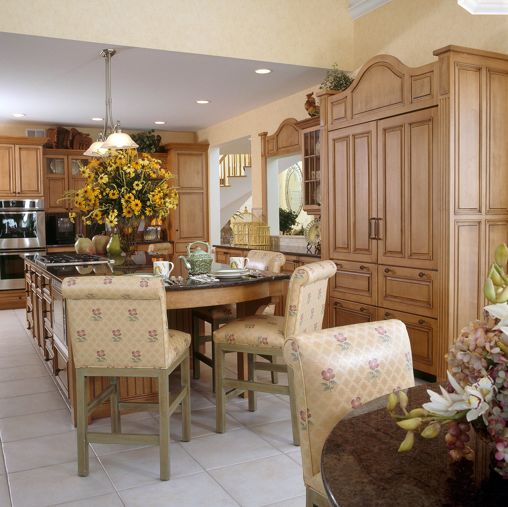 Klassisk inredning av ett kök, med rostfria vitvaror, en dubbel diskho, luckor med upphöjd panel, skåp i mellenmörkt trä, granitbänkskiva, beige stänkskydd, stänkskydd i stenkakel, klinkergolv i porslin och flera köksöar