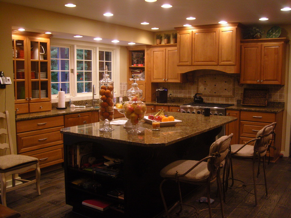 Photo of a medium sized traditional u-shaped kitchen/diner in Indianapolis with a submerged sink, raised-panel cabinets, brown cabinets, granite worktops, beige splashback, terracotta splashback, stainless steel appliances, medium hardwood flooring and an island.