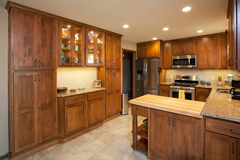 Inredning av ett klassiskt mellanstort kök, med en undermonterad diskho, luckor med infälld panel, skåp i mellenmörkt trä, bänkskiva i kvarts, vitt stänkskydd, stänkskydd i keramik, rostfria vitvaror, travertin golv och en halv köksö