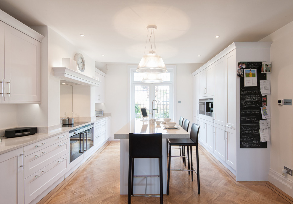 Klassische Küche mit Schrankfronten im Shaker-Stil, weißen Schränken, braunem Holzboden und Kücheninsel in London