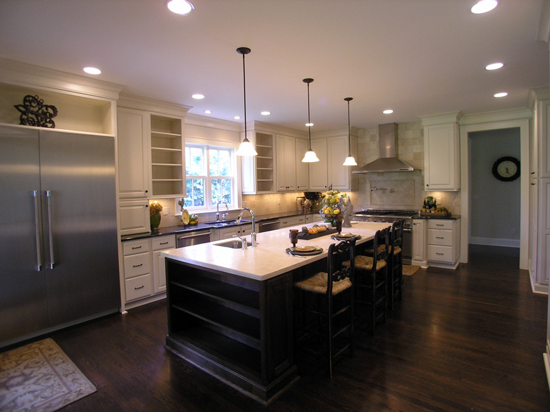 Example of a mid-sized classic l-shaped dark wood floor and brown floor open concept kitchen design in Kansas City with an undermount sink, raised-panel cabinets, white cabinets, beige backsplash, stone tile backsplash, stainless steel appliances and an island