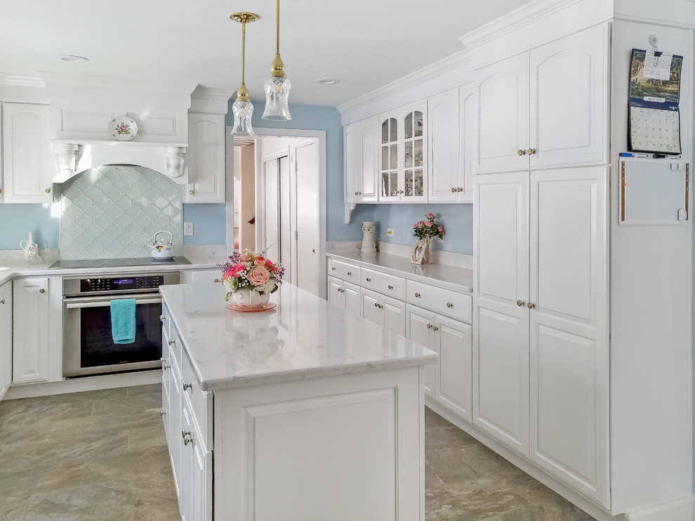 Photo of a medium sized classic galley enclosed kitchen in Boston with a double-bowl sink, raised-panel cabinets, white cabinets, engineered stone countertops, white splashback, glass tiled splashback, stainless steel appliances, porcelain flooring, an island and beige floors.