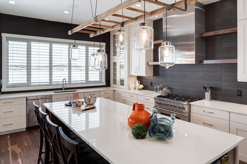 Klassische Küche in L-Form mit Unterbauwaschbecken, Küchenrückwand in Schwarz, Küchengeräten aus Edelstahl, Kücheninsel und braunem Holzboden in Calgary