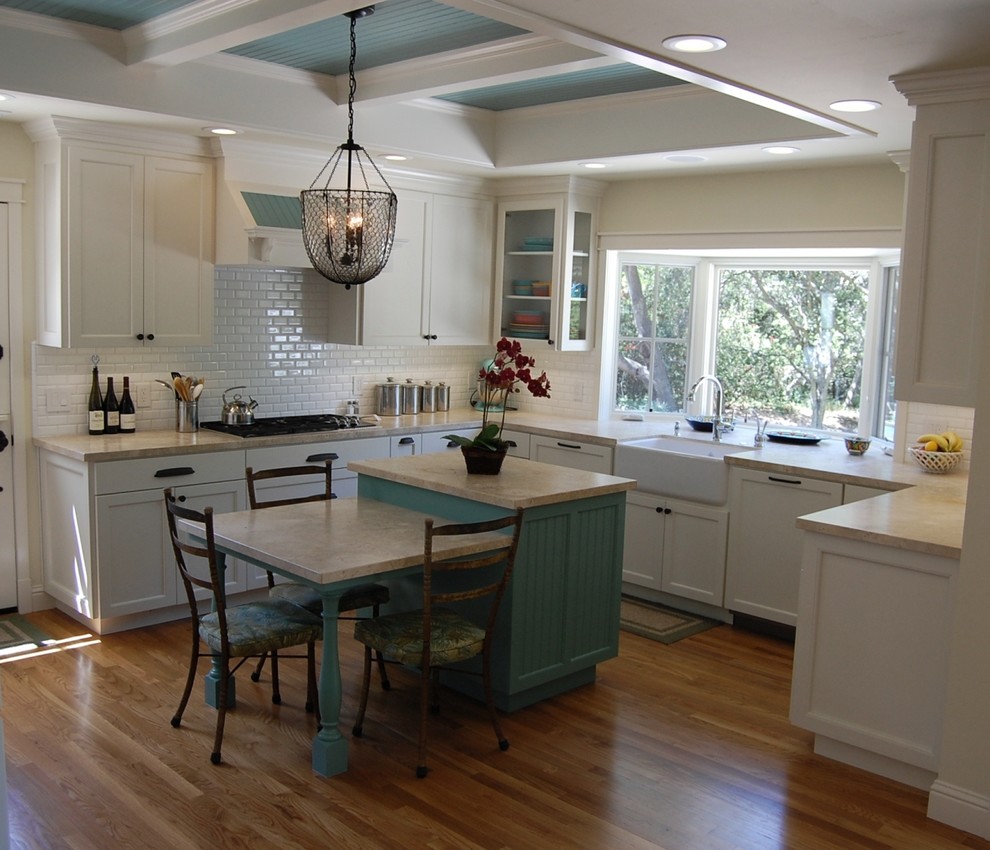 Mid-sized transitional u-shaped light wood floor eat-in kitchen photo in Orange County with a farmhouse sink, white cabinets, limestone countertops, white backsplash, subway tile backsplash, white appliances, an island and shaker cabinets