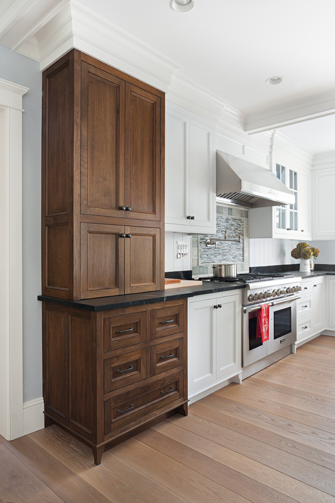 Design ideas for a classic l-shaped enclosed kitchen in Boston with a submerged sink, beaded cabinets, dark wood cabinets, soapstone worktops, stainless steel appliances, light hardwood flooring, an island, black splashback and stone slab splashback.