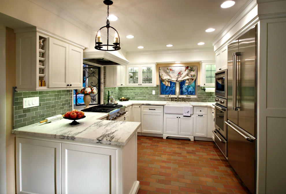 フェニックスにある中くらいなカントリー風のおしゃれなキッチン (エプロンフロントシンク、シェーカースタイル扉のキャビネット、白いキャビネット、緑のキッチンパネル、サブウェイタイルのキッチンパネル、シルバーの調理設備、レンガの床、赤い床) の写真