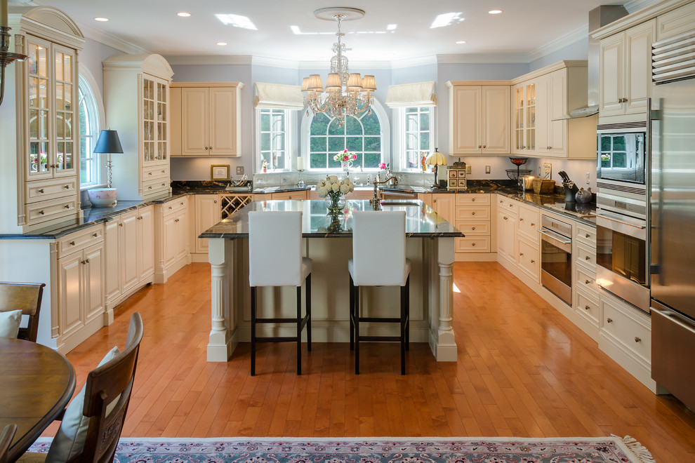 Cette photo montre une cuisine américaine chic en U avec des portes de placard beiges, un plan de travail en granite, une crédence noire et un électroménager en acier inoxydable.