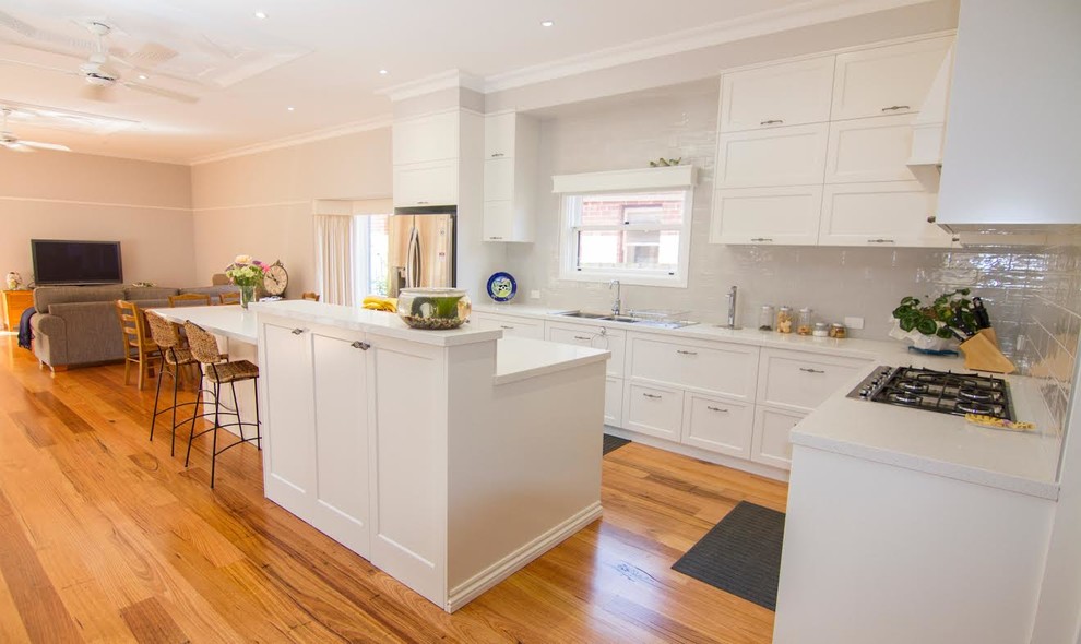 Inspiration for a medium sized traditional l-shaped open plan kitchen in Melbourne with shaker cabinets, white cabinets, an island, granite worktops, white splashback, porcelain splashback, a double-bowl sink, stainless steel appliances and medium hardwood flooring.
