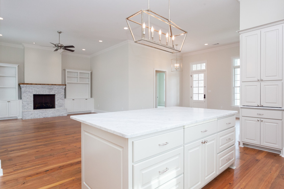 Mid-sized elegant l-shaped medium tone wood floor open concept kitchen photo in New Orleans with a drop-in sink, raised-panel cabinets, gray cabinets, marble countertops, white backsplash, ceramic backsplash, stainless steel appliances and an island
