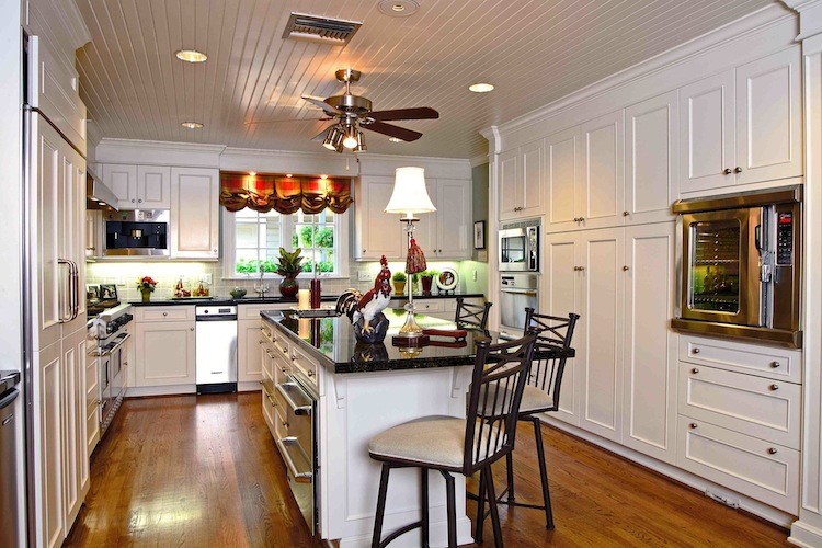 Klassisk inredning av ett mellanstort kök, med vita skåp, rostfria vitvaror, mellanmörkt trägolv, en undermonterad diskho, luckor med infälld panel, granitbänkskiva, vitt stänkskydd, stänkskydd i travertin, en köksö och brunt golv