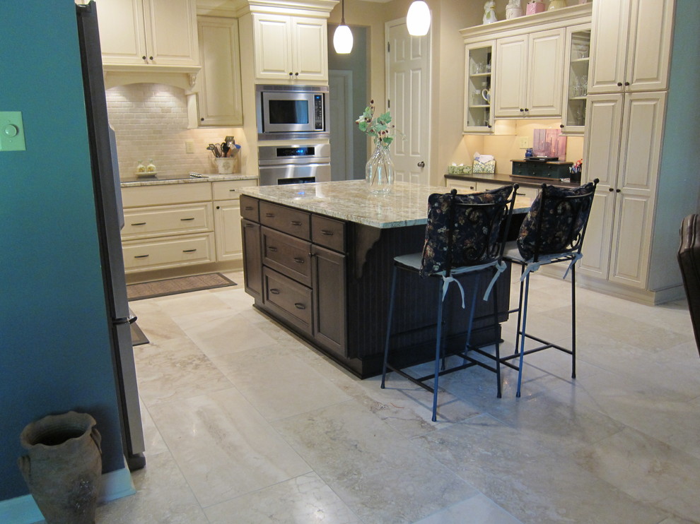Mid-sized elegant l-shaped travertine floor eat-in kitchen photo in Other with an undermount sink, glass-front cabinets, white cabinets, granite countertops, black backsplash, stone tile backsplash, stainless steel appliances and an island