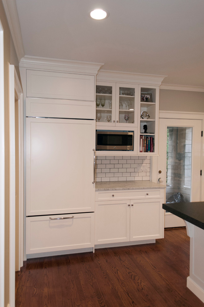 Photo of a medium sized traditional galley enclosed kitchen in New York with recessed-panel cabinets, white cabinets, marble worktops, white splashback, metro tiled splashback, stainless steel appliances, medium hardwood flooring and an island.