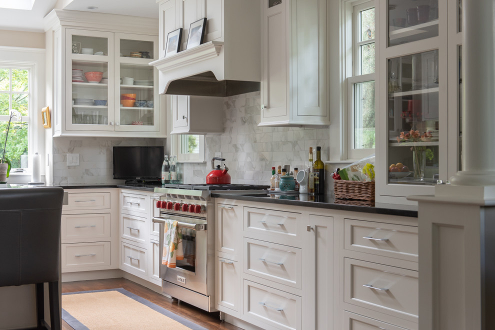 Große Klassische Küche mit Kassettenfronten, weißen Schränken, Küchenrückwand in Grau, Küchengeräten aus Edelstahl, braunem Holzboden, Kücheninsel, braunem Boden und schwarzer Arbeitsplatte in Boston