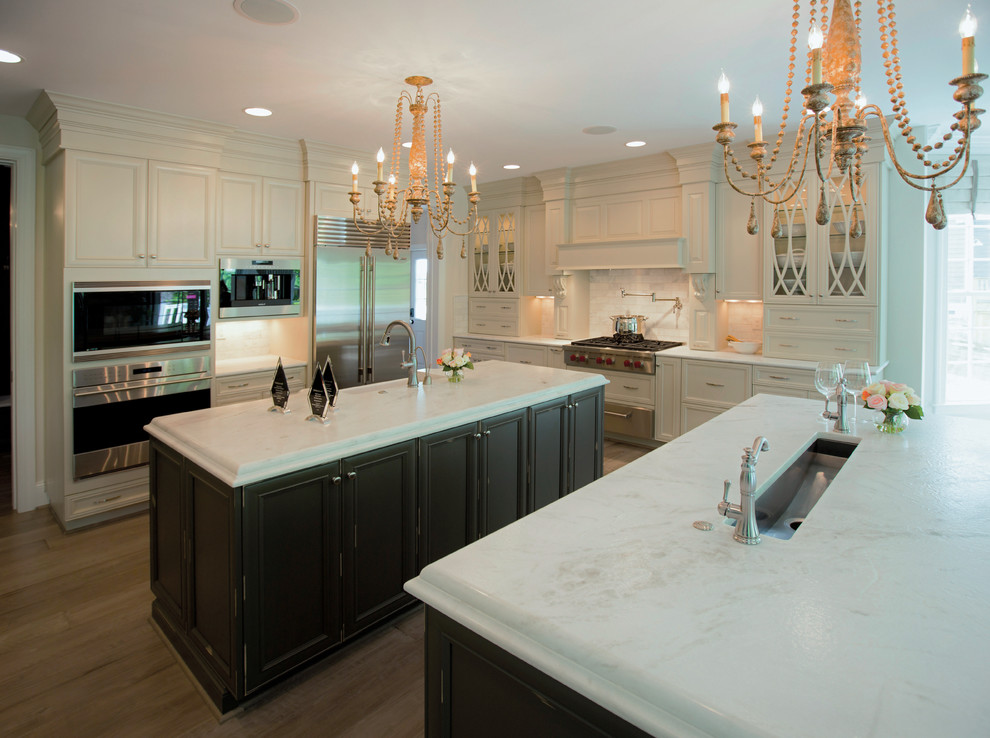Example of a large transitional u-shaped light wood floor eat-in kitchen design in Raleigh with a drop-in sink, shaker cabinets, white cabinets, quartz countertops, white backsplash, stone tile backsplash, stainless steel appliances and two islands