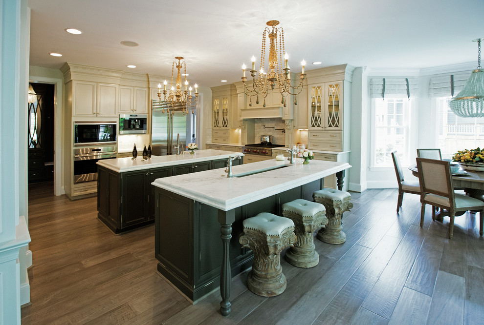 Eat-in kitchen - large transitional u-shaped light wood floor eat-in kitchen idea in Raleigh with a drop-in sink, shaker cabinets, white cabinets, quartz countertops, white backsplash, stone tile backsplash, stainless steel appliances and two islands