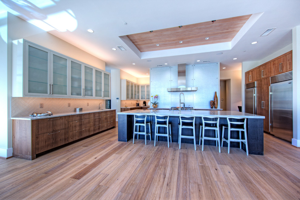 Cette image montre une grande cuisine américaine parallèle design en bois brun avec un évier encastré, un placard à porte plane, un plan de travail en granite, un électroménager en acier inoxydable, parquet clair et îlot.