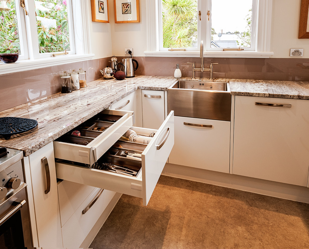 Mid-sized elegant u-shaped linoleum floor and gray floor eat-in kitchen photo in Auckland with white cabinets, granite countertops, glass sheet backsplash, stainless steel appliances, a farmhouse sink, flat-panel cabinets, brown backsplash and no island