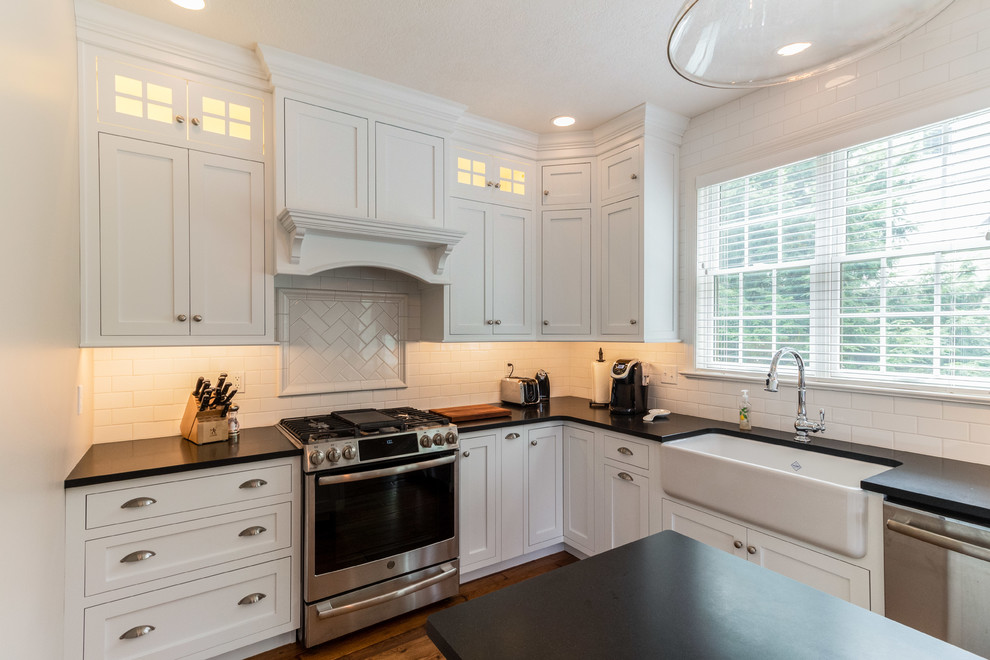 Example of a classic u-shaped dark wood floor and brown floor eat-in kitchen design in Philadelphia with a farmhouse sink, shaker cabinets, white cabinets, soapstone countertops, white backsplash, subway tile backsplash, stainless steel appliances, an island and black countertops