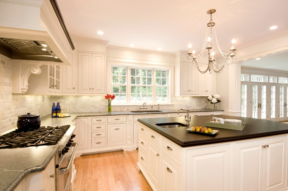 Inspiration for a mid-sized timeless u-shaped light wood floor enclosed kitchen remodel in Boston with an undermount sink, beaded inset cabinets, white cabinets, paneled appliances, an island, gray backsplash and subway tile backsplash