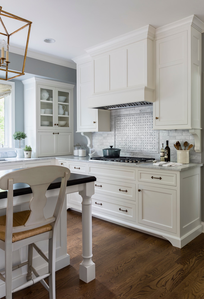 Inredning av ett klassiskt mellanstort kök, med en undermonterad diskho, luckor med infälld panel, vita skåp, marmorbänkskiva, vitt stänkskydd, stänkskydd i stenkakel, rostfria vitvaror, mellanmörkt trägolv och en köksö