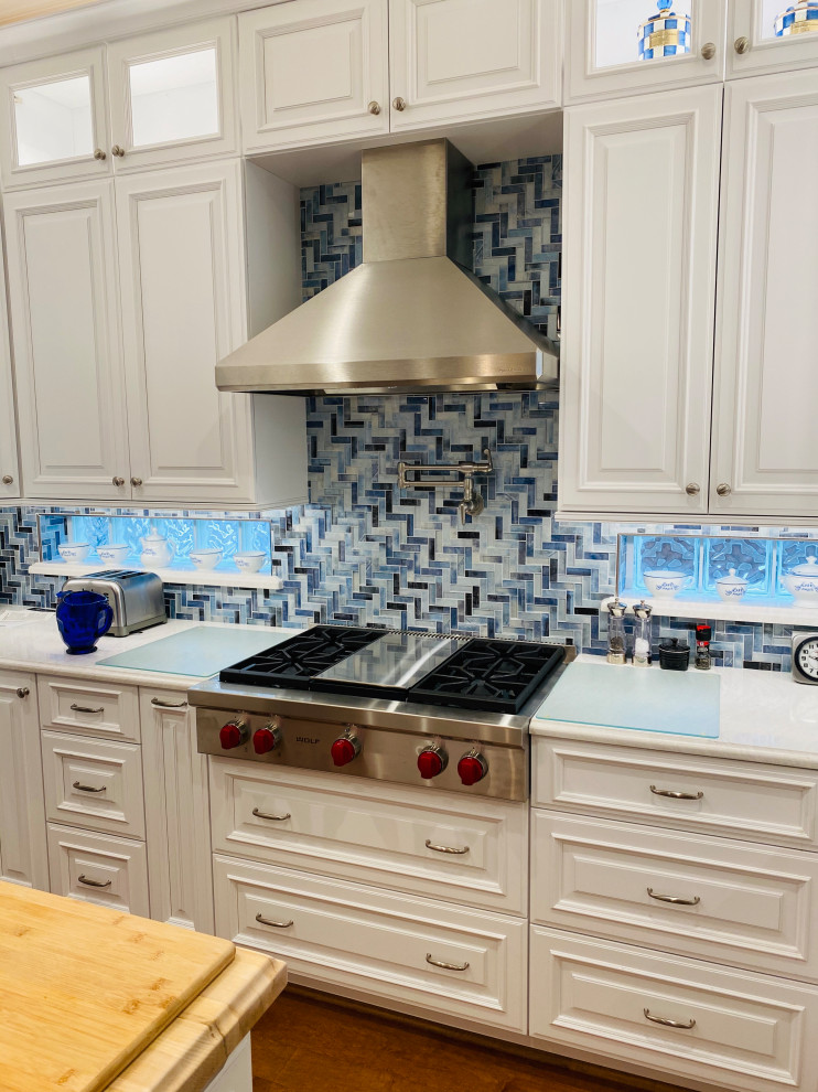 Inspiration for a large classic u-shaped open plan kitchen in Houston with a belfast sink, raised-panel cabinets, white cabinets, engineered stone countertops, blue splashback, mosaic tiled splashback, stainless steel appliances, medium hardwood flooring, an island, brown floors and white worktops.