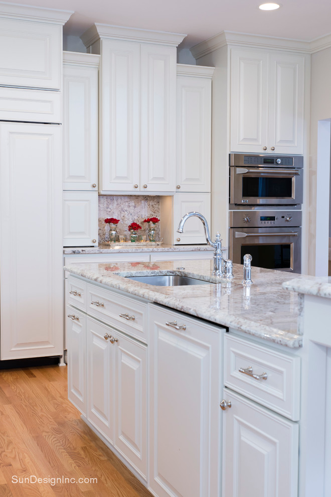 Bild på ett vintage kök, med en enkel diskho, luckor med profilerade fronter, vita skåp, granitbänkskiva, vitt stänkskydd, rostfria vitvaror, ljust trägolv och en köksö