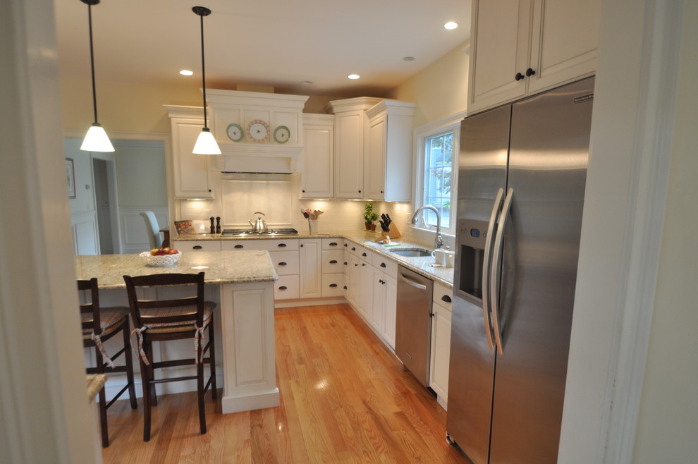 Example of a mid-sized classic medium tone wood floor open concept kitchen design in Boston with an undermount sink, raised-panel cabinets, white cabinets, granite countertops, beige backsplash, subway tile backsplash, stainless steel appliances and an island