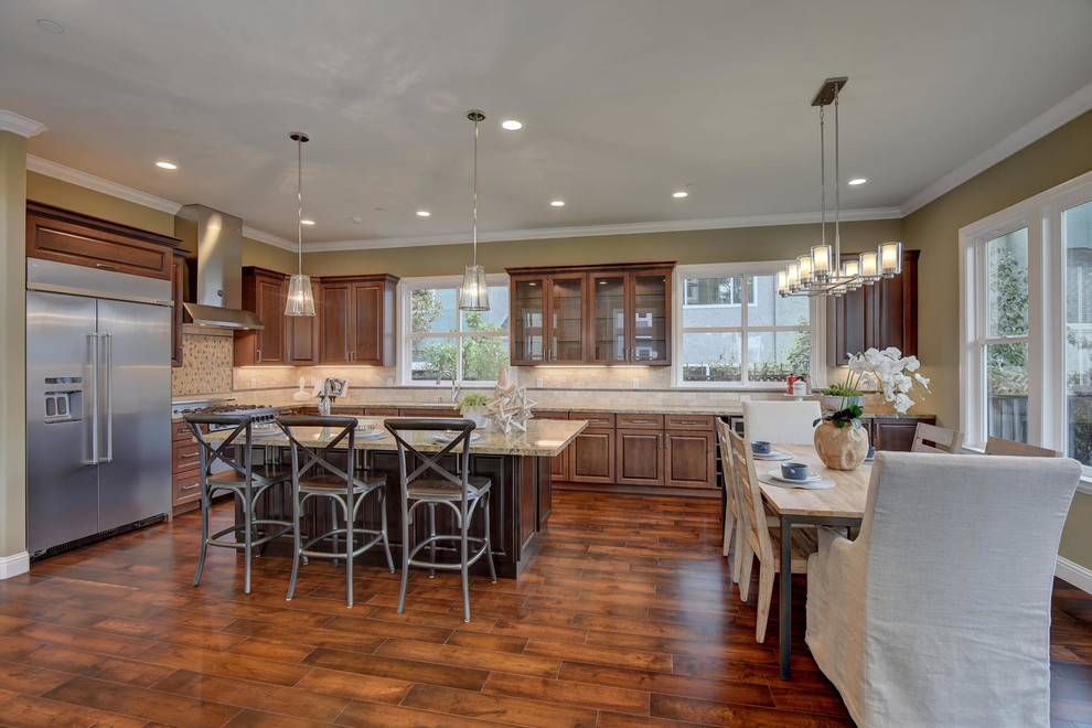 This is an example of a large traditional l-shaped kitchen/diner in San Francisco with a built-in sink, raised-panel cabinets, granite worktops, beige splashback, stainless steel appliances, medium hardwood flooring, an island, brown floors, travertine splashback and dark wood cabinets.