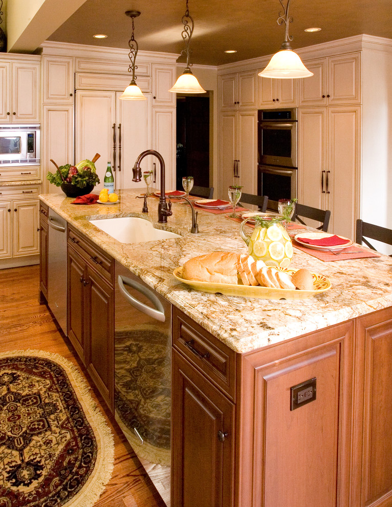 Eat-in kitchen - large traditional u-shaped medium tone wood floor eat-in kitchen idea in Chicago with an undermount sink, raised-panel cabinets, white cabinets, granite countertops, beige backsplash, stone tile backsplash, paneled appliances and an island