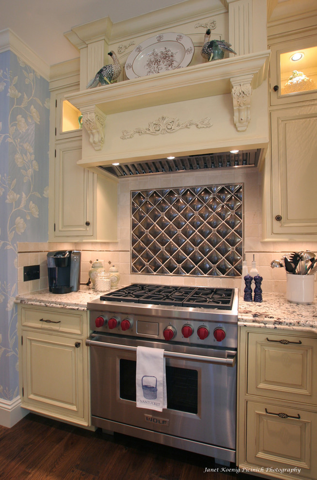 Klassische Küche mit Küchengeräten aus Edelstahl, profilierten Schrankfronten, beigen Schränken, Granit-Arbeitsplatte, Küchenrückwand in Metallic, Rückwand aus Metallfliesen und Tapete in Boston