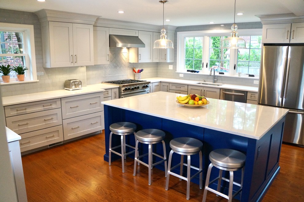 Bild på ett mellanstort vintage vit vitt kök, med en undermonterad diskho, skåp i shakerstil, blå skåp, bänkskiva i kvarts, blått stänkskydd, stänkskydd i keramik, rostfria vitvaror, mellanmörkt trägolv, en köksö och brunt golv