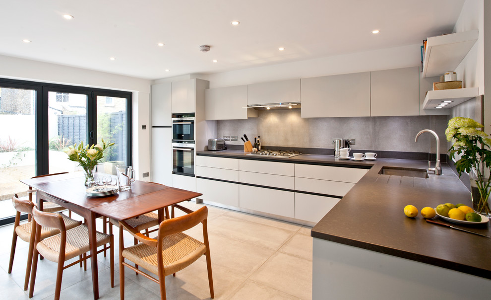 Moderne Wohnküche ohne Insel in L-Form mit Unterbauwaschbecken, grauen Schränken, Küchenrückwand in Grau, Rückwand aus Stein und Elektrogeräten mit Frontblende in Surrey