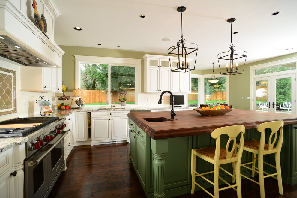 Inredning av ett klassiskt stort kök, med en undermonterad diskho, luckor med upphöjd panel, gröna skåp, träbänkskiva, vitt stänkskydd, stänkskydd i tunnelbanekakel, rostfria vitvaror, mellanmörkt trägolv och en köksö