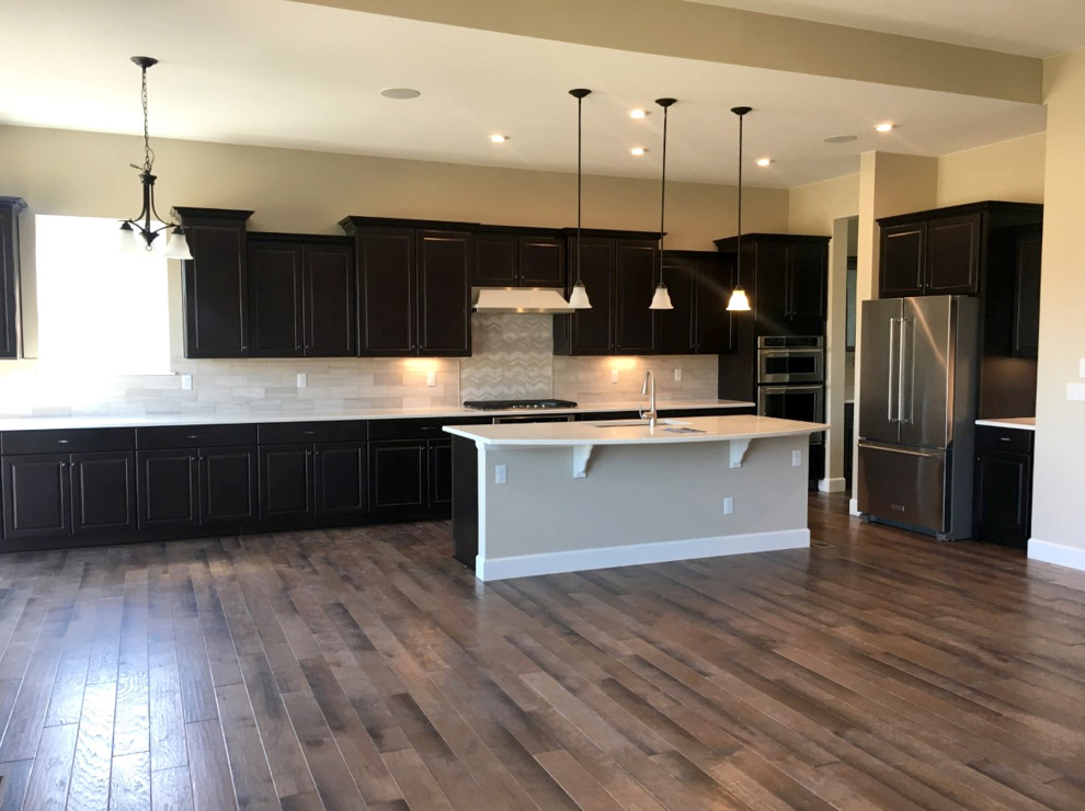 Kitchen - medium tone wood floor and brown floor kitchen idea in Denver with a single-bowl sink, raised-panel cabinets, dark wood cabinets, quartz countertops, limestone backsplash, stainless steel appliances, an island and white countertops