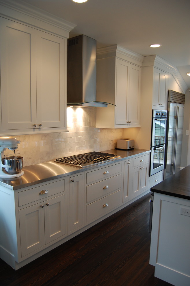 This is an example of a medium sized classic kitchen/diner in New York with a submerged sink, shaker cabinets, white cabinets, stainless steel appliances, dark hardwood flooring, an island, stainless steel worktops, white splashback and metro tiled splashback.