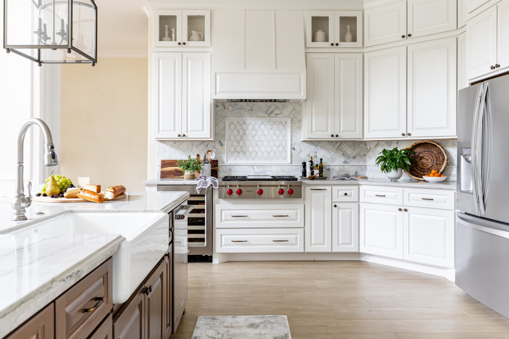 Klassisk inredning av ett grå grått l-kök, med en rustik diskho, luckor med upphöjd panel, vita skåp, grått stänkskydd, rostfria vitvaror, ljust trägolv, en köksö och beiget golv