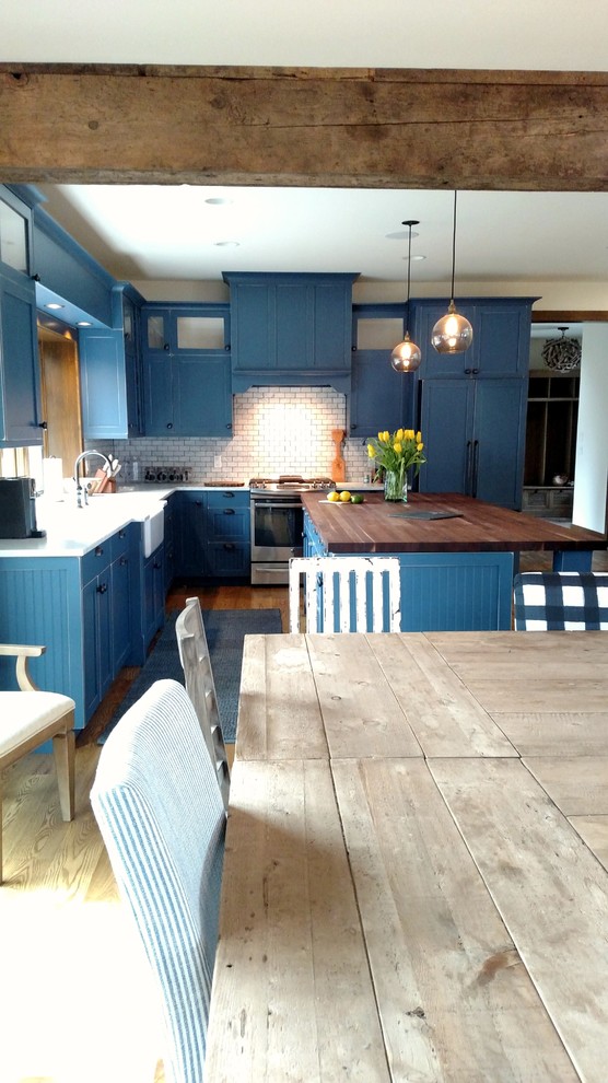 Large beach style l-shaped medium tone wood floor open concept kitchen photo in Boston with a farmhouse sink, shaker cabinets, blue cabinets, wood countertops, blue backsplash, subway tile backsplash, paneled appliances and an island
