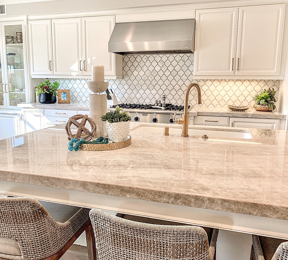 Trendy medium tone wood floor kitchen photo in Orange County with a triple-bowl sink, recessed-panel cabinets, white cabinets, quartzite countertops, white backsplash, marble backsplash, stainless steel appliances and an island