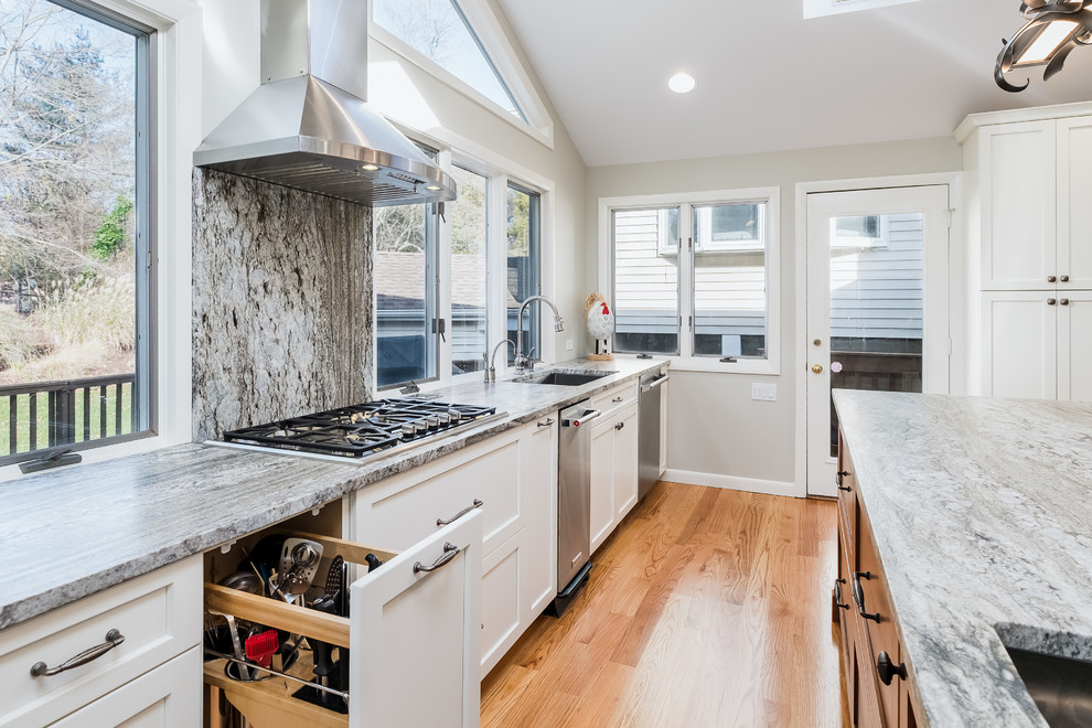 Inspiration for a huge contemporary l-shaped light wood floor open concept kitchen remodel in Bridgeport with an undermount sink, flat-panel cabinets, white cabinets, granite countertops, gray backsplash, stone slab backsplash, stainless steel appliances and an island